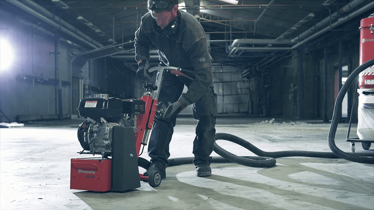 A man is utilizing a red and black concrete scarifying machine in a warehouse.